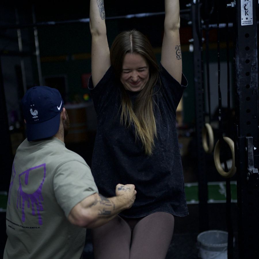 Le coach accompagne une adhérente à la barre de traction, tout sourire